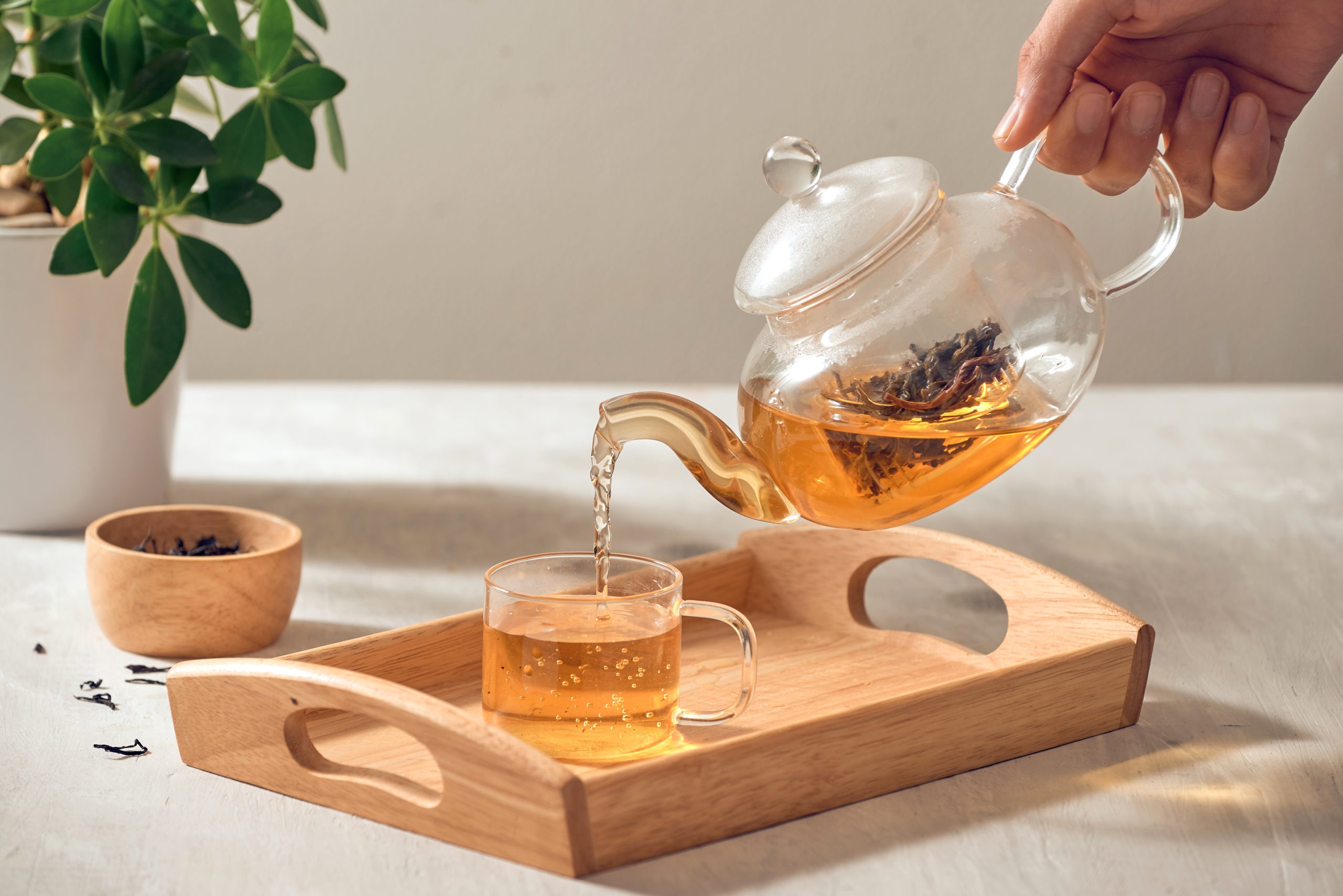 A hand pouring tea from glass teapot on wooden serving tray