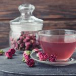 Tea rose flowers in glass jar and tea on wooden background
