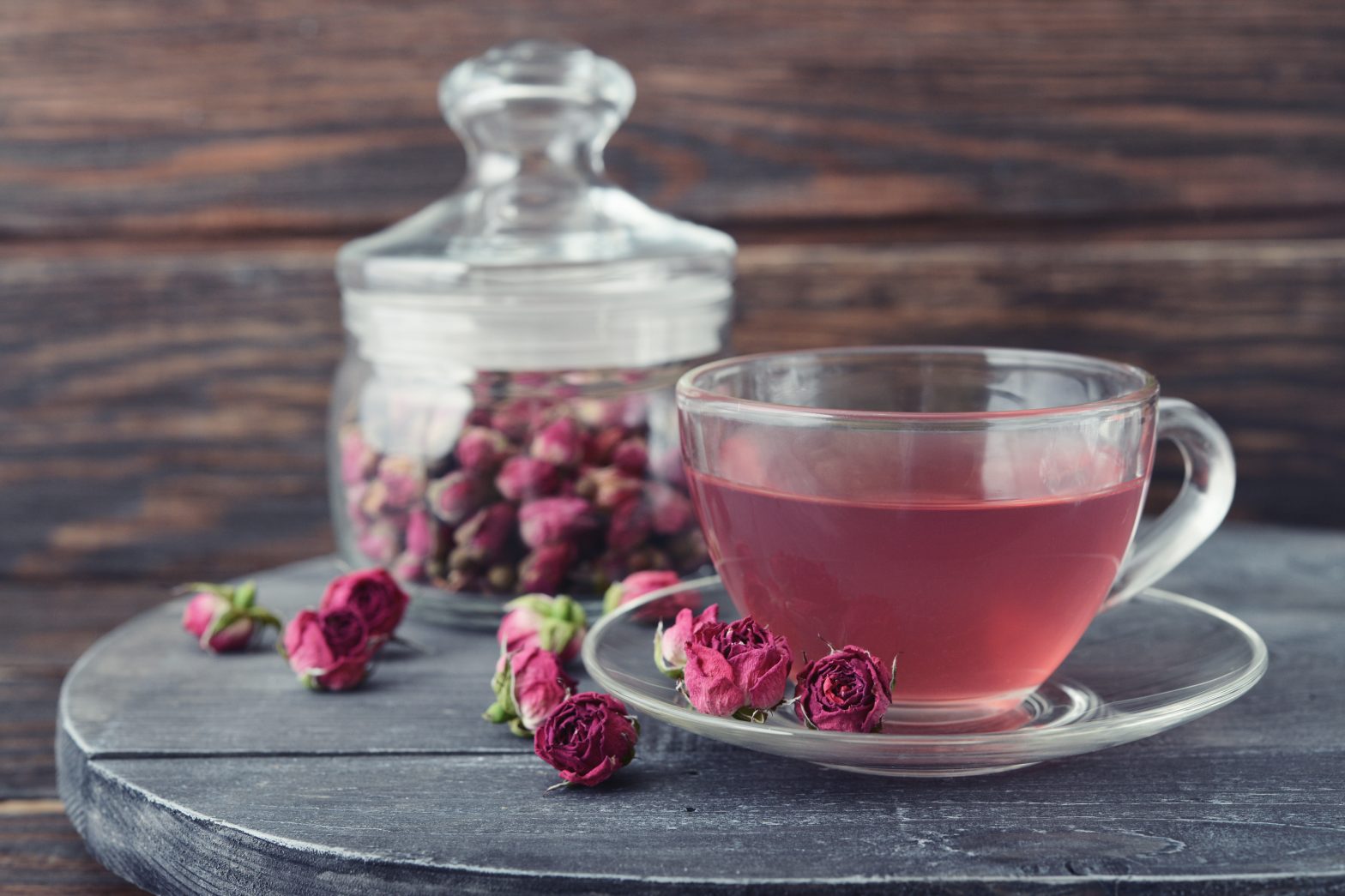 Tea rose flowers in glass jar and tea on wooden background