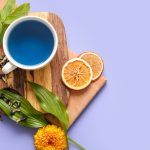 Cup of blue tea and dried butterfly pea flowers on color background