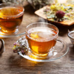 Cups of herbal tea and green tea with various herbs on wooden table