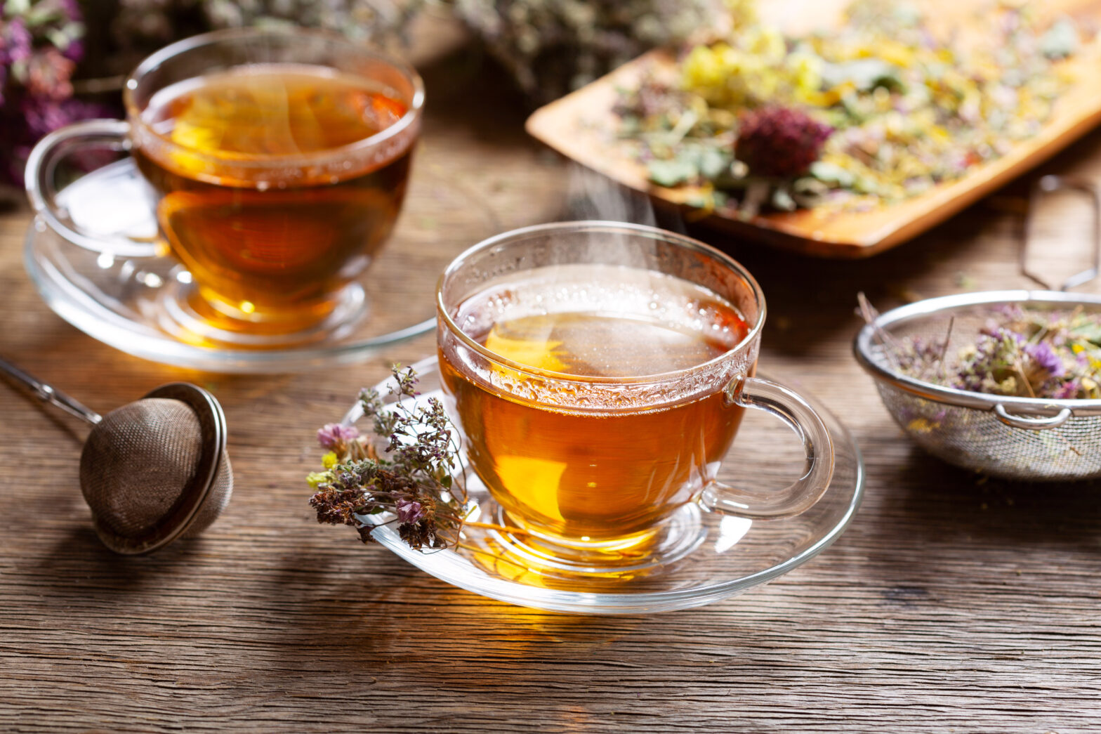 Cups of herbal tea and green tea with various herbs on wooden table