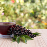 Glass cup of tasty elderberry tea and berries on wooden table