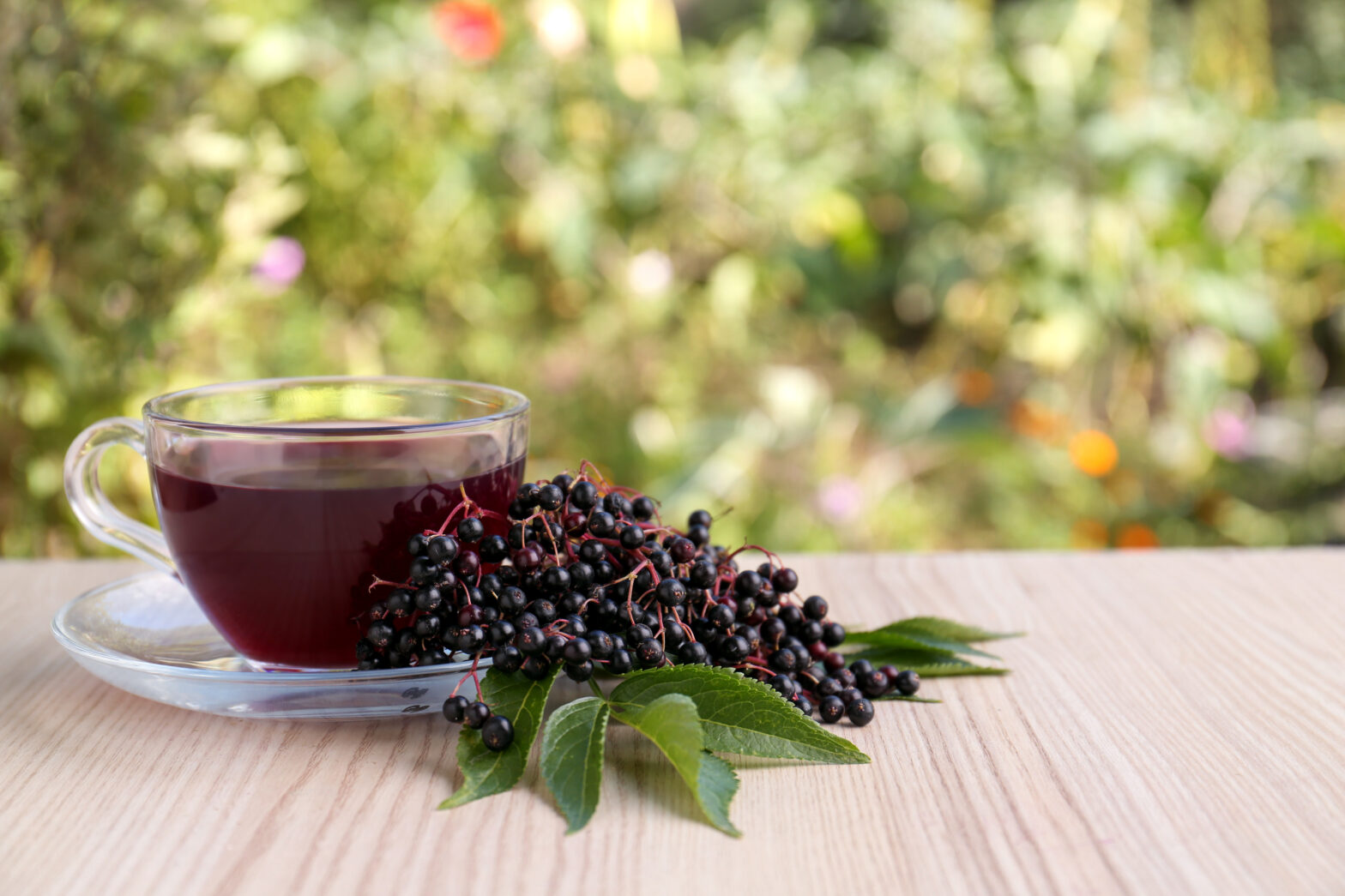 Glass cup of tasty elderberry tea and berries on wooden table