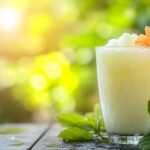 Glass of granita tea down the glass, sitting on a wooden table with blurred green plants and vibrant flowers softly framing the garden