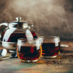 Transparent teapot and two glass cups with black tea on a table