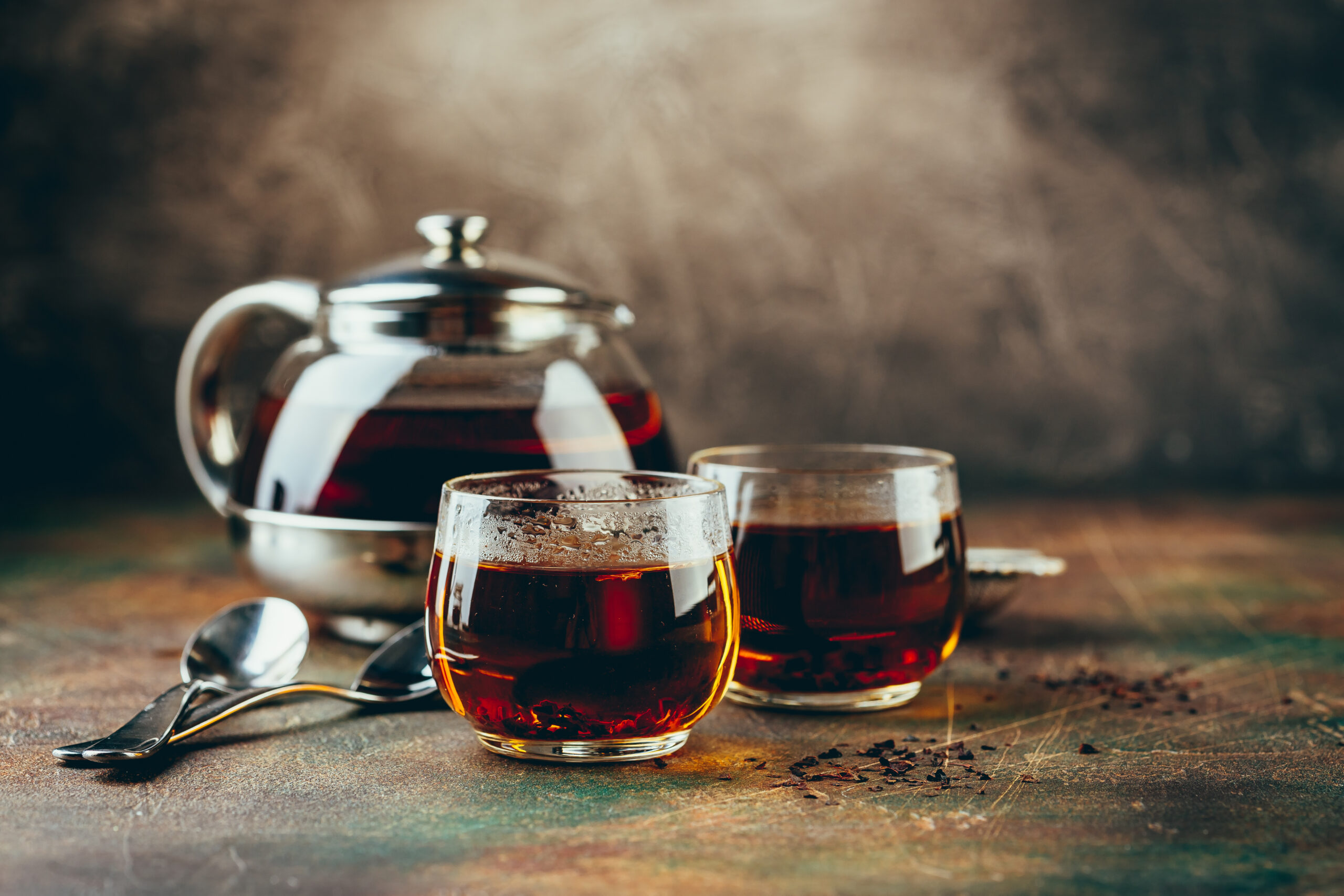 Transparent teapot and two glass cups with black tea on a table